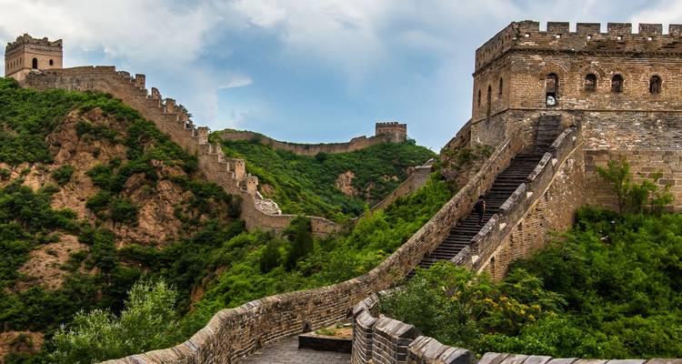 Un tramo majestuoso de la Gran Muralla China se serpentea sobre crestas verdes y exuberantes bajo un cielo dramático.