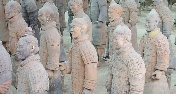 Filas de estatuas de guerreros de terracota a tamaño natural están de pie en un pozo de excavación con iluminación tenue.