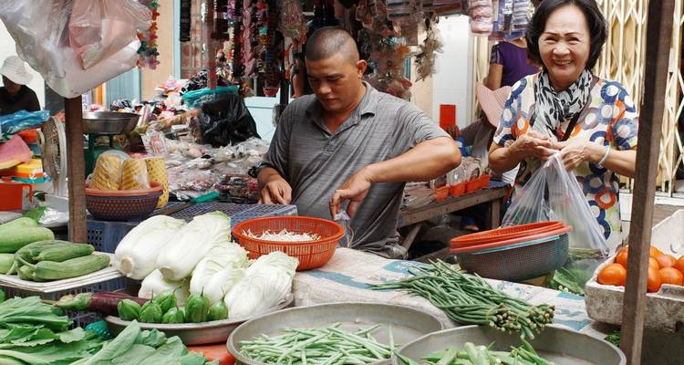 Des vendeurs souriants préparant des produits frais à un étal de marché humide vietnamien.