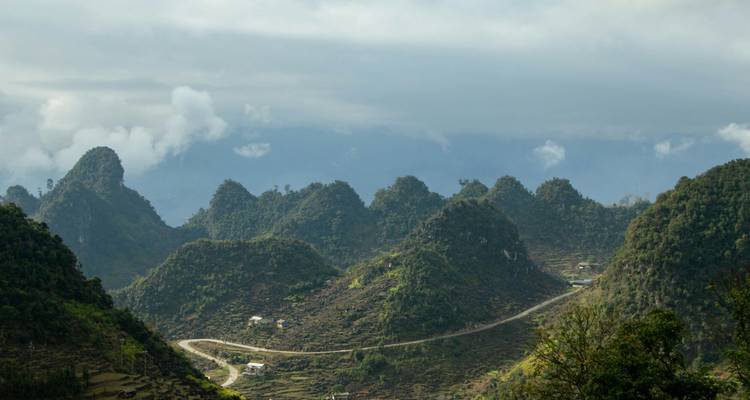 Les pics karstiques ondulants avec une route de montagne sinueuse sous un ciel nuageux créent un paysage accidenté.