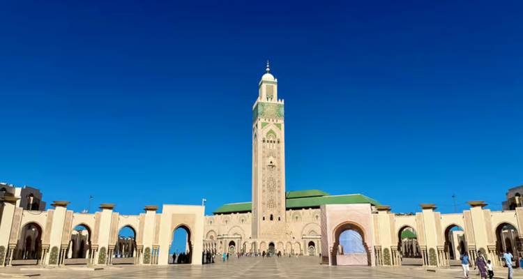 The soaring minaret of Hassan II Mosque rises over a spacious courtyard against a deep blue sky.