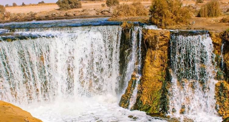 Brede waterval die over een rotsachtige rand in een woestijnoase-omgeving naar beneden stort