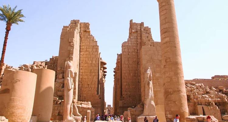 Los visitantes caminan entre las imponentes ruinas de arenisca y estatuas del Templo de Karnak bajo un cielo despejado.