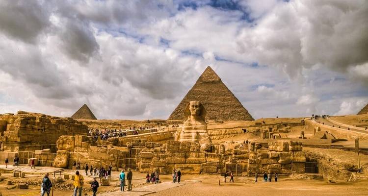 Menigten verkennen het Sphinx- en pyramidecomplex onder een dramatische bewolkte hemel.