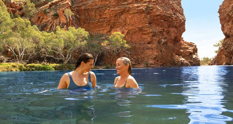 Deux femmes profitent d'une baignade rafraîchissante dans les eaux cristallines d'une gorge aux roches rouges.