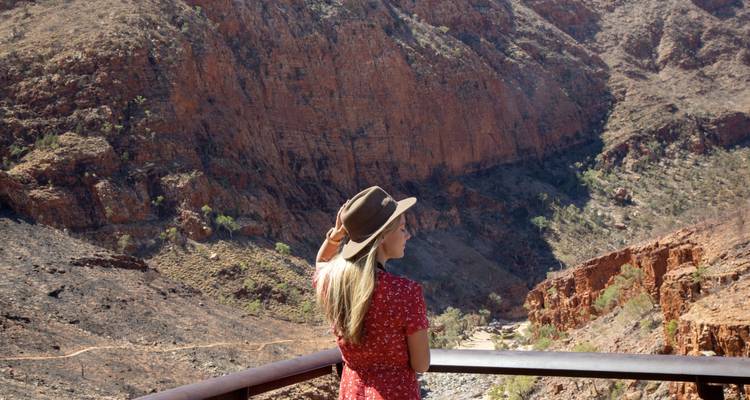 Un voyageur vêtu d'une robe rouge et d'un chapeau admire les murs escarpés d'un canyon du désert profond.