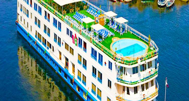 A brightly painted multi-deck Nile cruise ship with rooftop pool sails on calm blue water.