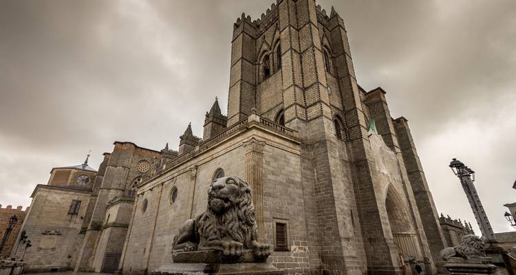 Catedral de piedra de aspecto sombrío con escultura de león en primer plano bajo cielos nublados