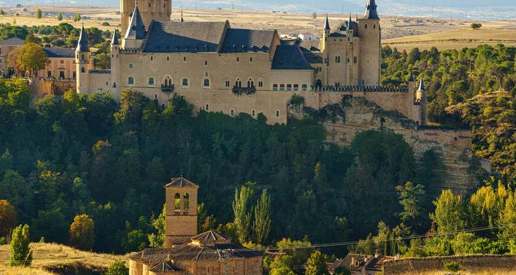 Castillo de cuento de hadas tipo Alcázar que se eleva sobre un desfiladero boscoso y llanuras ondulantes
