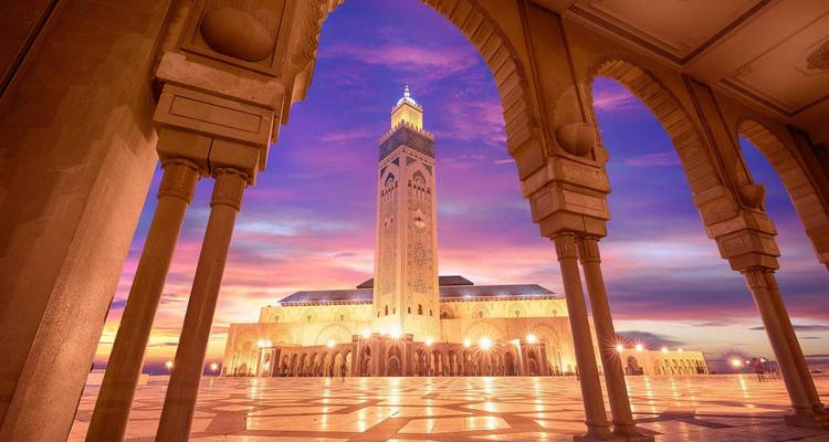 Hassan II Mosque in Casablanca framed by ornate arches glows against a dramatic sunset sky.