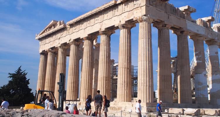The Parthenon’s majestic columns rise against a blue sky while visitors explore the base