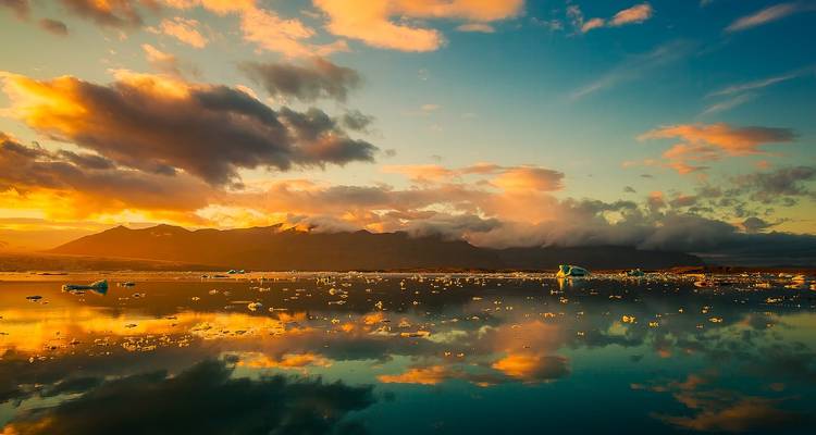 El atardecer dorado se refleja en una laguna glaciar cristalina salpicada de icebergs bajo unas nubes espectaculares en Islandia