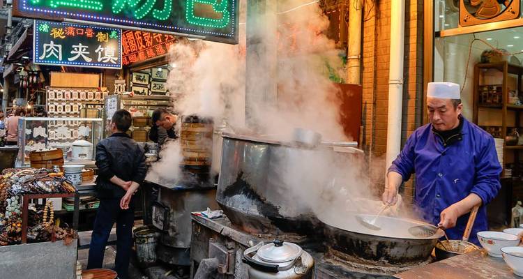 Dampf steigt von einem geschäftigen chinesischen Straßenverkaufsstand für Speisen in einer lebhaften Marktgasse auf.