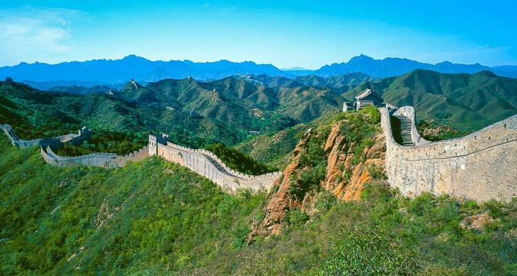 Die Chinesische Mauer, die sich durch grüne Berge unter einem klaren blauen Himmel schlängelt