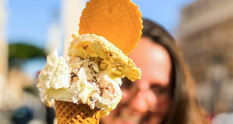 Nahaufnahme eines farbenfrohen italienischen Gelato-Eises in einer Waffel, das von einer lächelnden Person im Hintergrund gehalten wird