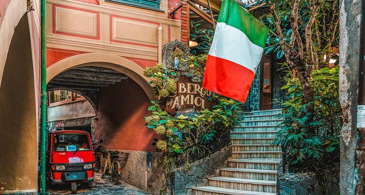 Malerische italienische Gasse mit Nationalflagge, Pflanzen und einem winzigen roten dreirädrigen Lastwagen