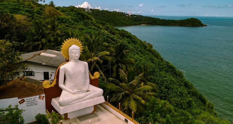 Große weiße Buddha-Statue mit Blick auf dichte grüne Küstenlinie und Meer