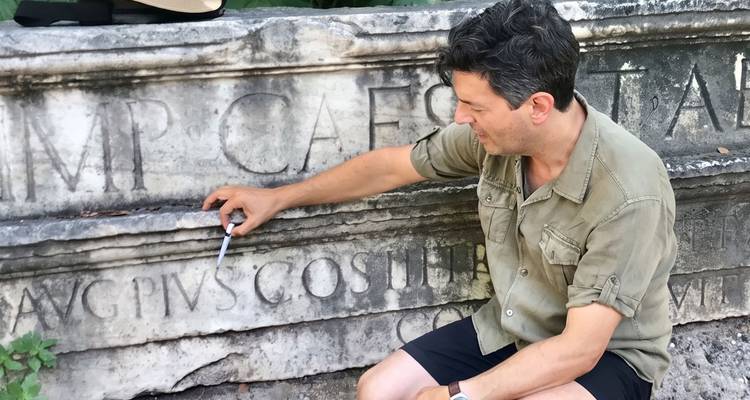 Guide points out Latin inscriptions on an ancient marble monument outdoors.