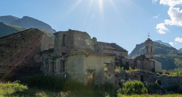 Sunlight beams over abandoned stone houses in a mountain valley.