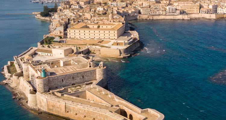 Aerial view of the historic island of Ortigia surrounded by clear blue Mediterranean waters.