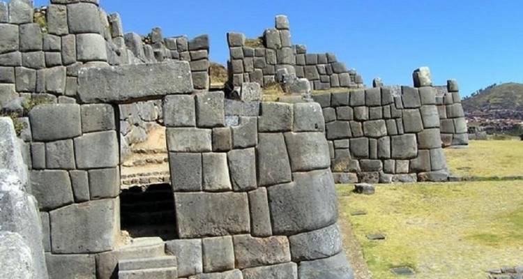 Massive interlocking Incan stone walls of Sacsayhuaman rise against a clear blue Andean sky.