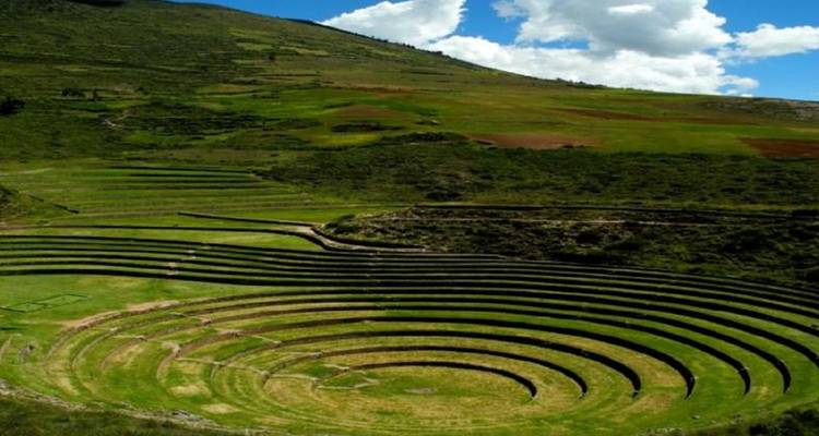 Concentric agricultural terraces of Moray form dramatic green rings beneath a partly cloudy sky.
