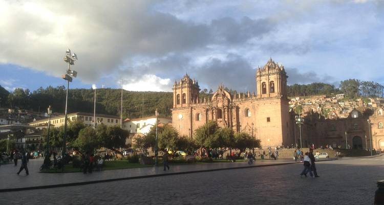 Bustling Plaza de Armas in Cusco with imposing cathedral façades framed by dramatic late-day clouds.