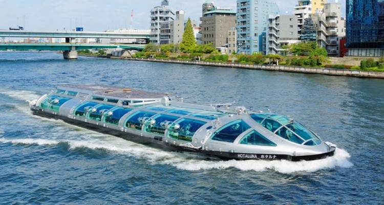 Futuristic glass-roofed riverboat cruising down an urban waterway flanked by modern buildings and bridges.