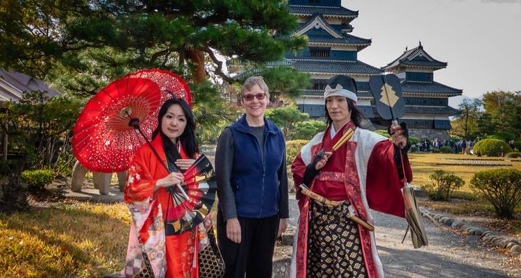 Tourist poses with performers in samurai costume in front of a historic Japanese castle.