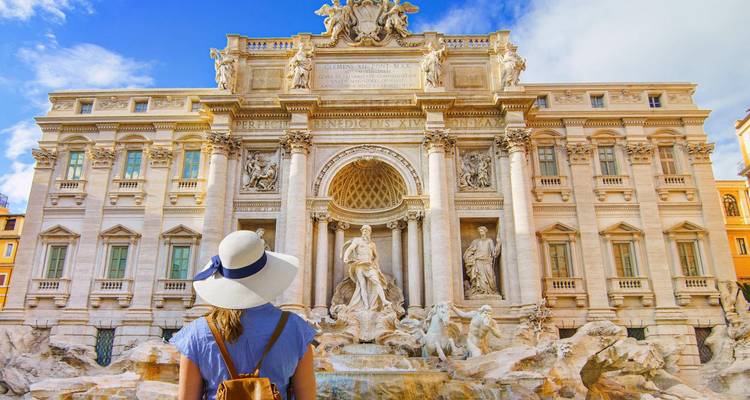 Back-view of a woman in sunhat admiring the ornate marble façade of Rome’s Trevi Fountain.