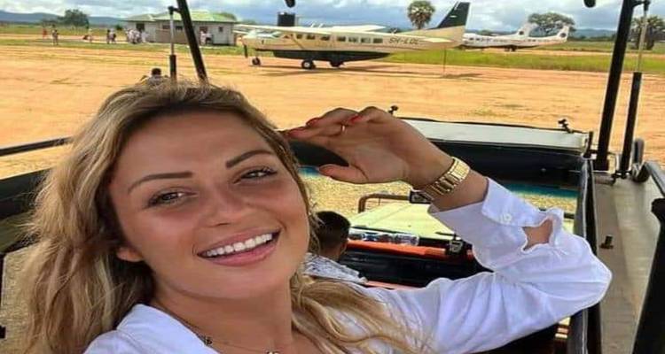 Smiling traveler taking a selfie from an open safari vehicle with small aircraft on a dusty runway in the background.