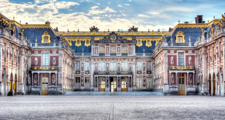 Symmetrical front façade of Versailles Palace glowing with gilded details beneath a pastel sky.
