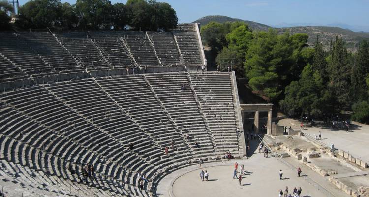 Sweeping stone tiers of the ancient Theatre of Epidaurus surrounded by pine trees and distant mountains.