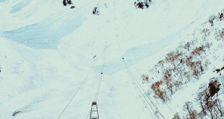 Met sneeuw bedekte bergafhelling met kabelbaan torens die vervagen in witte uitgestrektheid