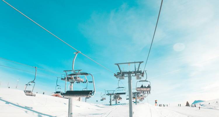 Stoeltjesliften die skiërs over een stralende sneeuwhellingen onder een heldere blauwe hemel vervoeren