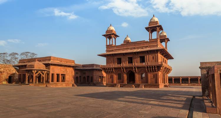 Empty courtyard and red-sandstone pavilion of Fatehpur Sikri’s palace complex beneath a blue sky.