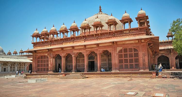Red sandstone arcaded mosque courtyard at Fatehpur Sikri under a bright blue sky.