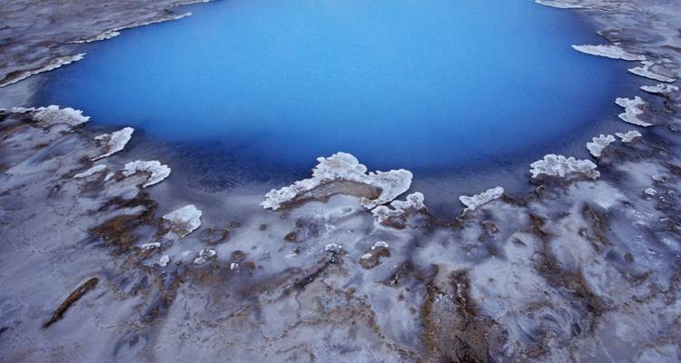 Vue aérienne d'une piscine géothermale d'un bleu éclatant bordée de dépôts minéraux.