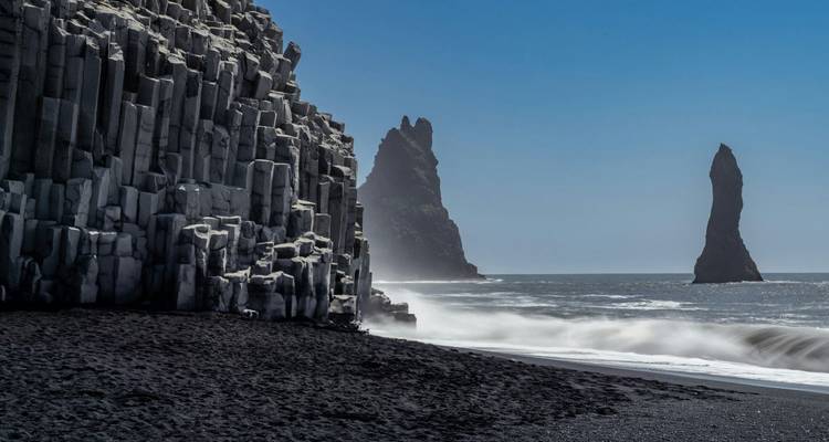 Les cheminées basaltiques et la plage de sable noir de Reynisfjara avec des vagues qui se brisent sur le rivage.