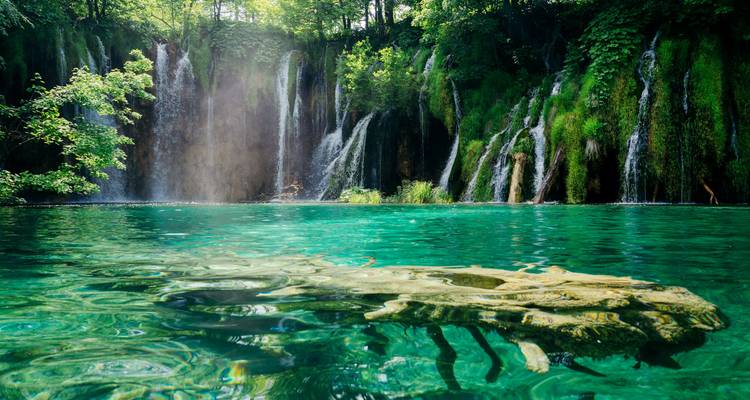 Kristallklarer Smaragdpool unter üppigen Wasserfällen in einem bewaldeten Nationalpark