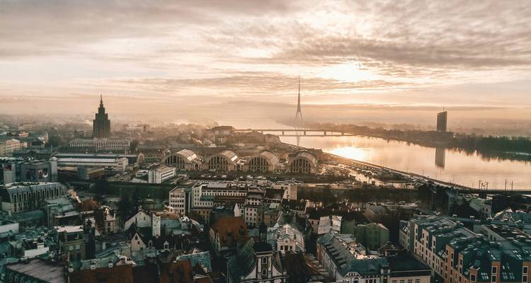 Golden sunrise casts warm glow over a riverfront European city with bridges and distinctive TV tower.