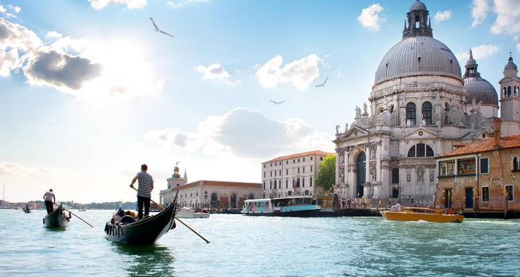 Gondoleros conduciendo góndolas por el Gran Canal de Venecia pasando la Basílica de Santa María della Salute con su cúpula bajo el brillante sol.