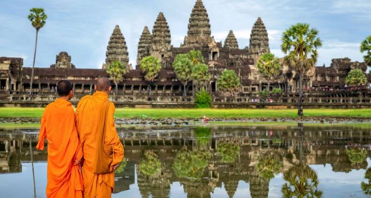 Dos monjes budistas con túnicas naranjas observan el reflejo de Angkor Wat en un estanque tranquilo.