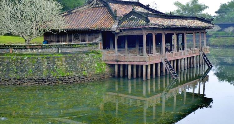Ein traditioneller hölzerner Pavillon auf Stelzen spiegelt sich in stillem grünem Wasser innerhalb der kaiserlichen Anlage.