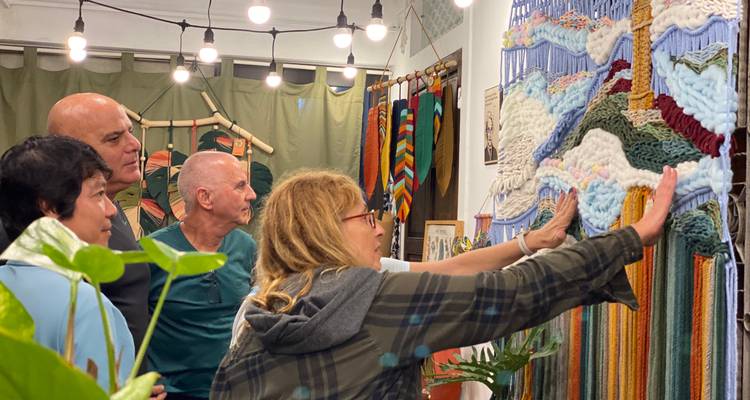 Eine kleine Gruppe studiert ein farbenfrohen gewebten Textil, das in einem künstlerischen Studio hängt, unter Anleitung einer lokalen Handwerkerin.