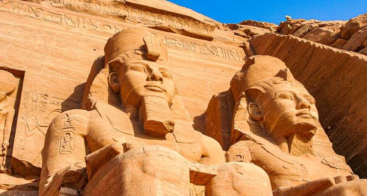 Monumentales estatuas de arenisca de faraones bañadas en luz cálida bajo un cielo azul.