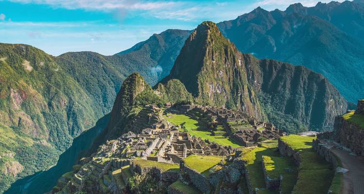 Ikonische Inkastadt Machu Picchu, eingebettet zwischen steilen grünen Andengipfeln unter klarem Himmel.