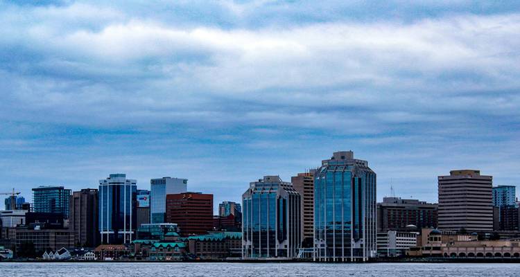 Modern skyline of Halifax with glass office towers viewed across grey harbour waters beneath clouded skies.