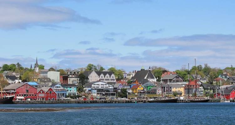 Colourful wooden waterfront buildings of a coastal Nova Scotia town seen from across calm blue water.