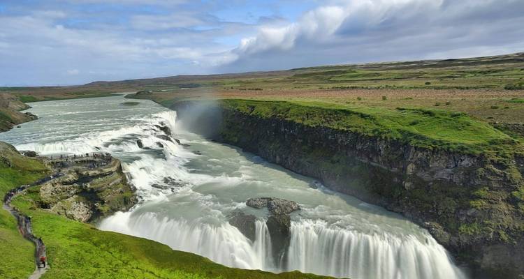 Vue aérienne de la puissante cascade de Gullfoss à plusieurs étages qui se jette dans un canyon verdoyant avec la brume formant un arc-en-ciel.